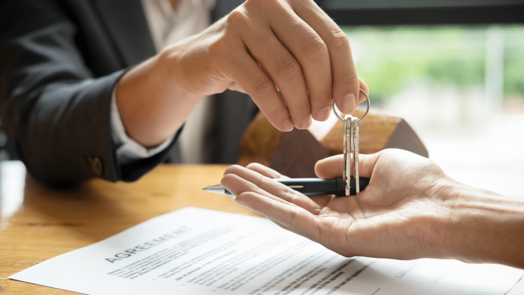 Agente inmobiliario certificado entregando las llaves de una propiedad para comprar. Una mano reciben y un contrato abajo.
