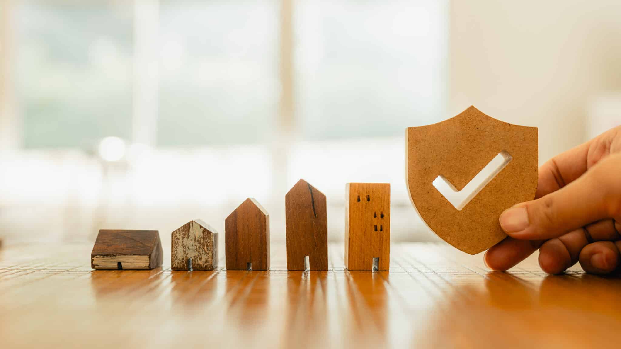 Wooden house model and real estate insurance ideas, and small shield icon. Housing insurance against impending loss and fire, building fire insurance concepts.